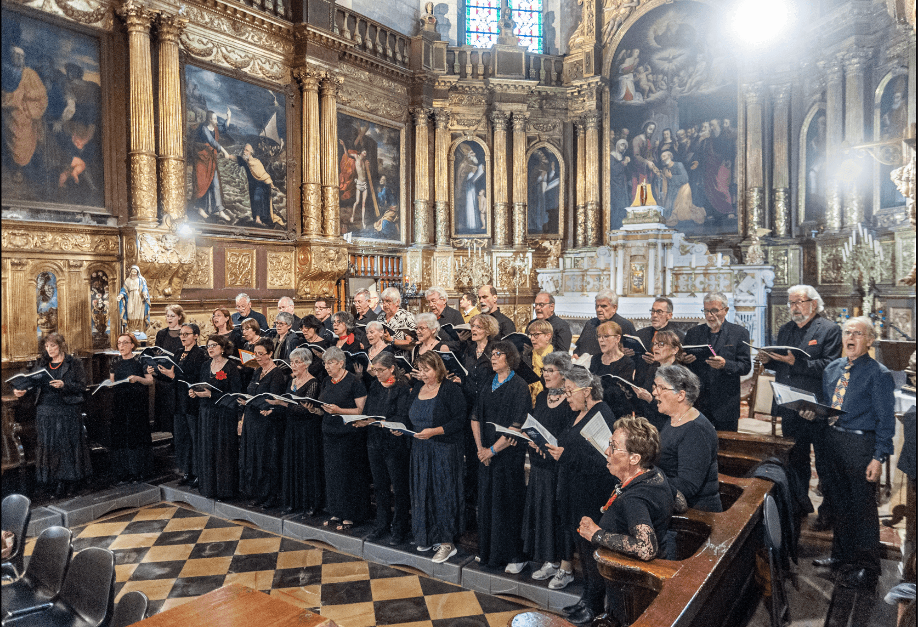 Ensemble Vocal d'Avignon en train de chanter dans une eglise d'Avignon de style baroque, tous vetus de noir. Diverses peintures murales sont visibles